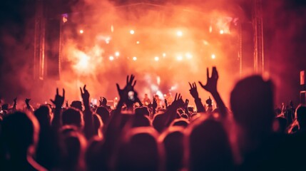 A crowd of people with their hands raised at a concert with a stage and spotlights in the background.