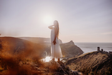 woman stands on a hill overlooking the ocean, her arms raised in the air. Concept of freedom and joy, as if the woman is celebrating a moment of happiness or accomplishment.