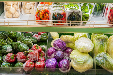 A variety of vegetables are on display in a store, including green peppers, red peppers, and cabbage