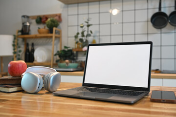 Laptop with blank screen, headphone, apple and books on wooden kitchen counter