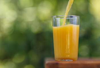 orange juice pouring in glass on wooden table outdoors