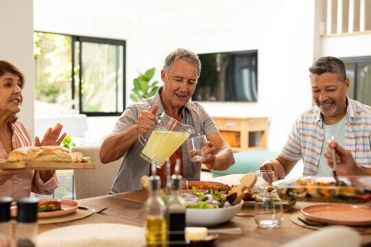 Pouring lemonade into glass, senior diverse friends enjoying meal together at home, at home