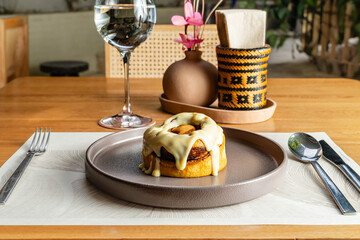 Spongy and exquisite cinnamon roll with sweet white sauce drizzled. Elegant hotel restaurant, gastronomy and desserts.