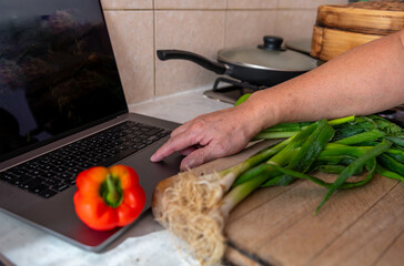 A person using a laptop computer in the kitchen to help with cooking by following an online recipe. A technology use concept.