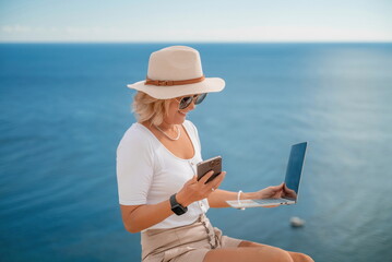 Freelance women sea working on the computer. Good looking middle aged woman typing on a laptop keyboard outdoors with a beautiful sea view. The concept of remote work.