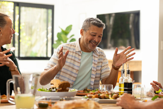 Enjoying meal, senior diverse friends laughing and talking around dining table, at home