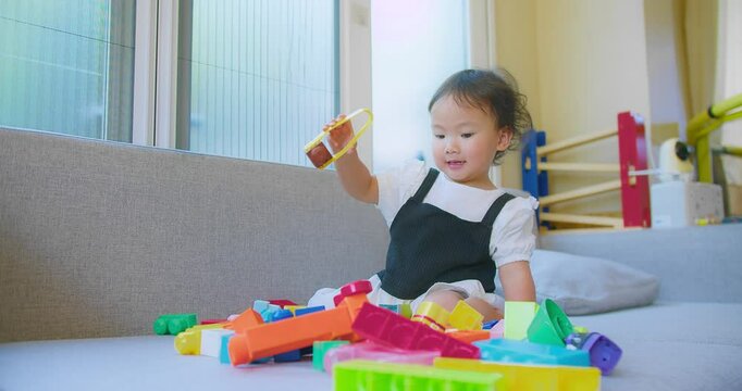 A young child girl engaged in creative play with vibrant building blocks in a sunlit living room, fostering imagination and development.