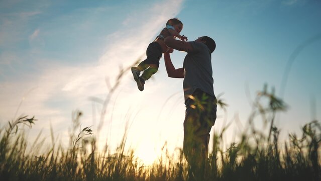 father playing with son in the park. happy family kid dream concept. father throws baby up silhouette in summer at sunset. parent and child play toss up silhouette outdoors in the park lifestyle