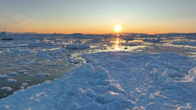 Sunset in Greenland nature. Aerial view of setting sun and pieces of melted icebergs. Glaciers melting, global warming, arctic nature landscape
