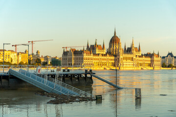 Fototapeta premium Budapest, Hungary - September 19, 2024: The parliament building in sunset golden light. Danube river overflowed its banks on the foreground.