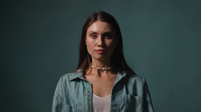 On gray blue background in studi portrait of beautiful woman look on camera serious. Light and shadow. Posing