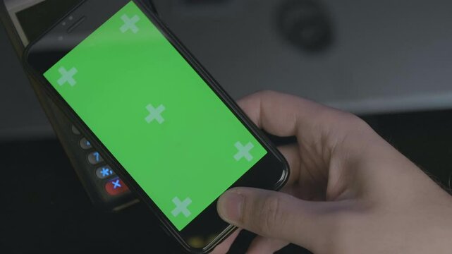 Top view of person using contactless payment with smartphone. Green screen template on phone.