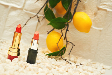 Red pink lipsticks on yellow pebbles stones with lemon branch