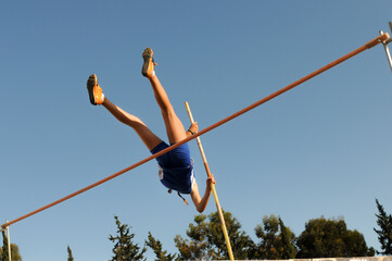 Female pole vaulter clearing the bar under blue sky