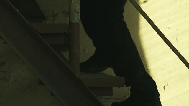 SWAT forces operator in black gear walking up a rusty old staircase in an abandoned warehouse