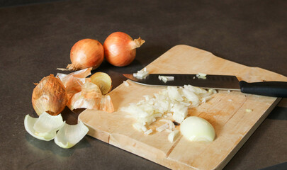 Close up of cutted white onion on a wooden board with a knife, grey kitchen table 
