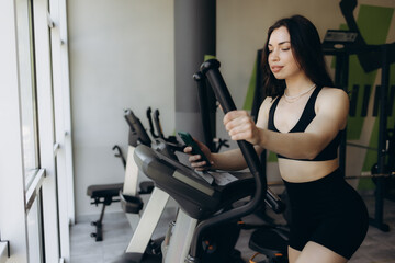 Fototapeta premium Beautiful young woman doing cardio on a stationary bike while smiling