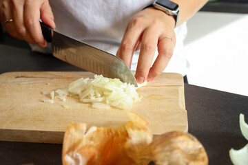 Close up of female hands cutting raw onions on wooden board, blurry background 