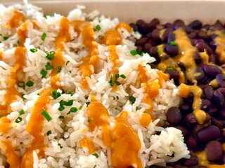 Close-up of a vegan dish from Vibe Kitchen in Dana Point, California, featuring rice and black beans topped with a vibrant orange sauce and garnished with fresh green herbs.