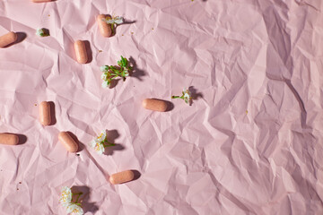 Blister packs with capsules scattered on a textured pink background, alongside small white flowers.