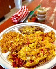 Plate of Mexican food featuring scrambled eggs, cheese, rice, beans, and sauces on a table in San Marcos, California.