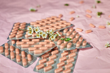 Blister packs with capsules scattered on a textured pink background, alongside small white flowers.