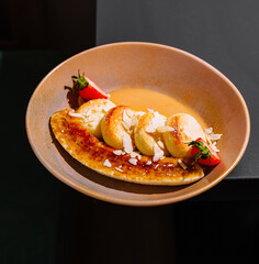 Delicious cottage cheese pancakes lying on caramelized banana with strawberries and almonds in restaurant