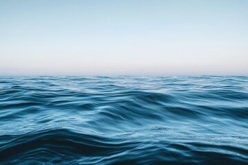 Obraz premium Gentle blue ocean waves ripple across a calm sea surface under a clear sky at the horizon