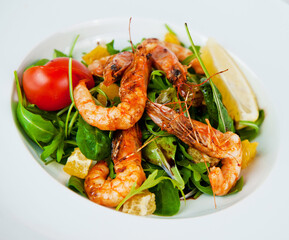 Delicious salad with grilled shrimps, arugula and orange slices on white plate