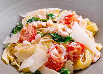 Pasta fettuccine with shrimps, spinach, cherry tomatoes and parmesan cheese on black background
