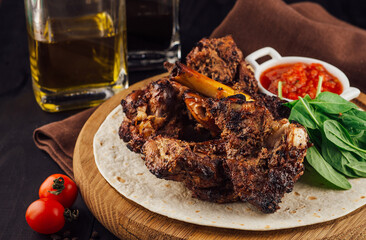 Grilled lamb ribs served on tortilla with spinach and sauce on wooden board