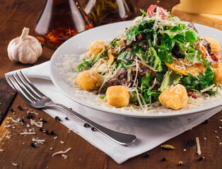 Fresh salad with meat and croutons being served on a wooden table
