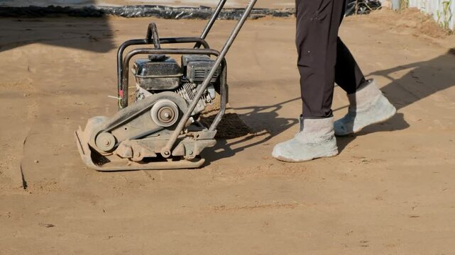 Worker operating vibration ramming machine for compaction of soil at a construction site. Construction and renovation