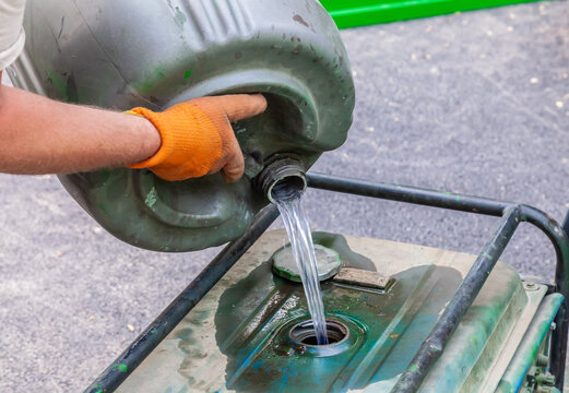 Pours gasoline from a barrel. A worker fills the generator with fuel.