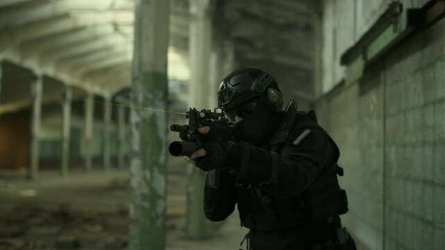 Portrait follow shot of a SWAT operator in black gear and an assault rifle with a green laser securing an abandoned warehouse