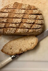 A loaf of freshly sliced bread with seeds on top, placed next to a knife on a rustic wooden surface, showcasing a wholesome and homemade feel