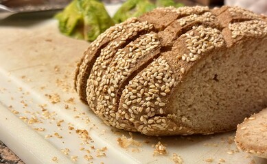 A close-up of a sliced loaf of sesame seed bread on a cutting board, with fresh lettuce in the background, creating a wholesome and appetizing scene