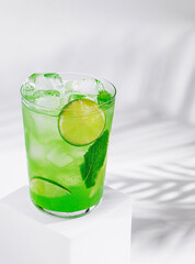 Refreshing green cocktail with lime and mint standing on white cube