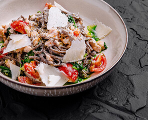 Black spaghetti with salmon, spinach and parmesan cheese lying on dark stone background