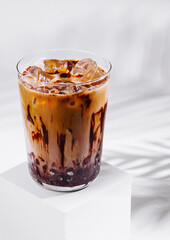 Iced coffee with chocolate syrup standing on white cube with palm leaf shadow