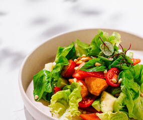 Fresh vegan salad with lettuce, tomatoes, avocado, and pine nuts on white table