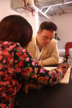 Woman assisting man with Down Syndrome in office