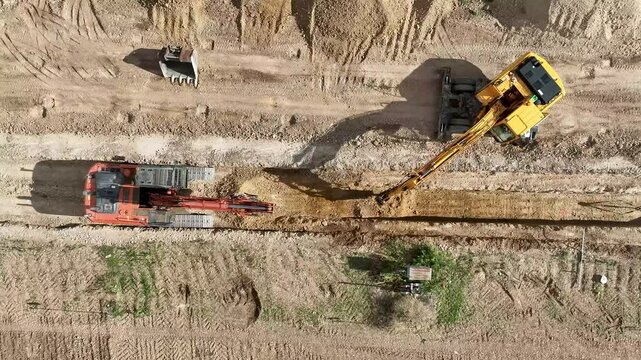 Top view video of two backhoes working together excavating a trench in a construction site
