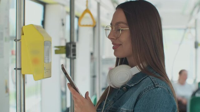Portarit of a young smiling woman paying conctactless with smartphone for the public transport in the tram.