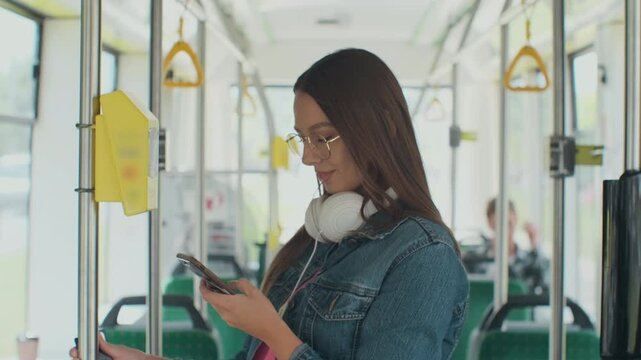 Portarit of a young smiling woman paying conctactless with smartphone for the public transport in the tram.