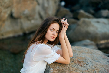 serene beauty young woman sitting gracefully on a rock by the sea, contemplating the horizon