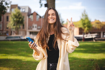 Happy brunette woman hold mobile phone posing on park background. Outdoor shot of happy lady show...