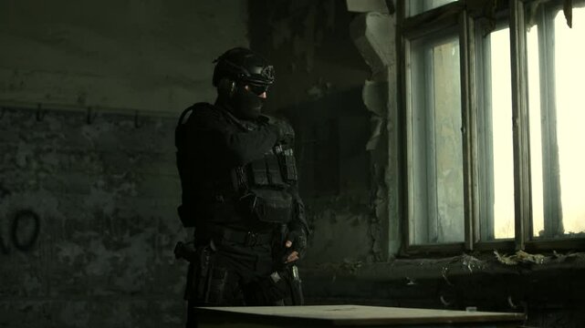 SWAT operator in black military gear flipping and fidgeting with a knife in an abandoned building