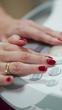 Adult female hands with red manicure and ring manage the buttons on the equipment panel. Close up. Medic working on ultra sound machine.