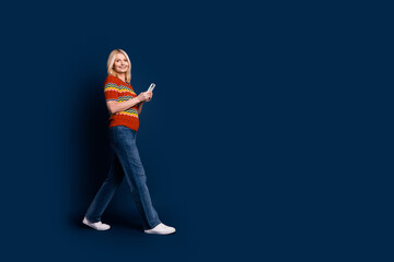 Photo of positive lovely senior woman wear stylish clothes use gadget walk empty space isolated on dark blue color background